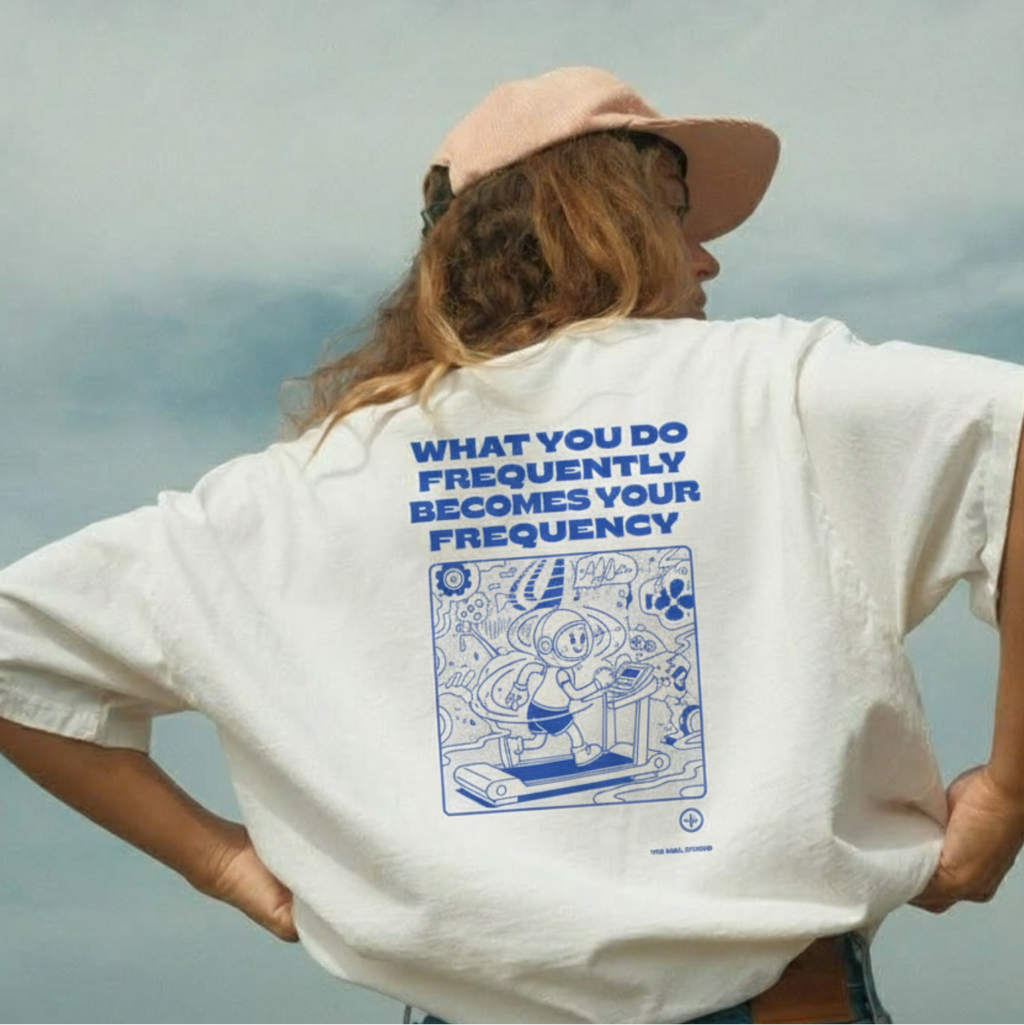 Person wearing a white t-shirt with a blue graphic and text, standing against a cloudy sky.